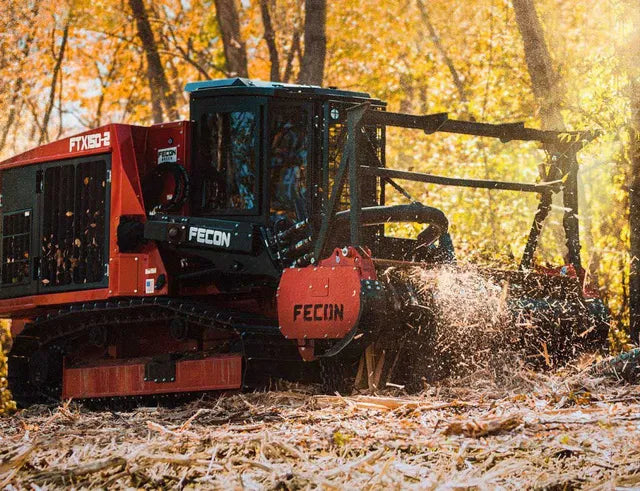 A Fecon forestry mulcher is seen on an autumn day, shredding wood and clearing brush amongst yellow and brown tree foliage.
