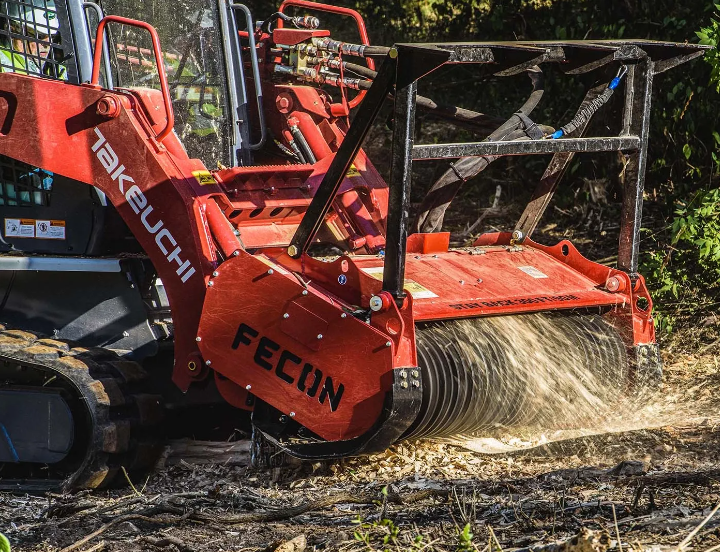 A red Takeuchi machine with a Fecon attachment is clearing land, chipping and grinding foliage and debris.